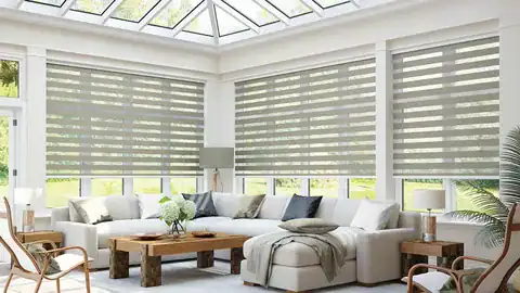 Bright sunroom with large windows, striped blinds, and comfortable white sectional sofa.