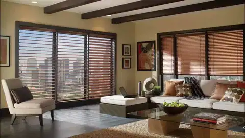 Bright living room with large windows, wooden blinds, city skyline view, stylish furniture.