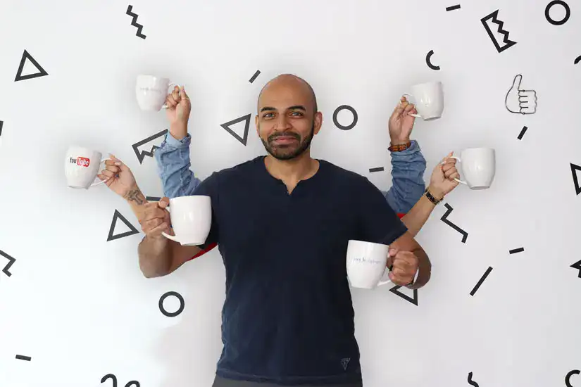 Multiple coffee cups held by a smiling man with social media icons on the wall behind him.