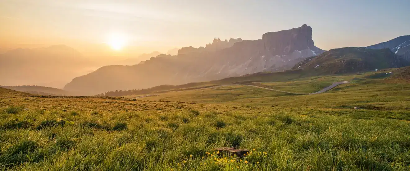Sunrise over rolling green hills and rugged mountains in a scenic outdoor setting.