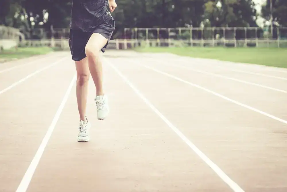 Athlete running on a track, focusing on legs and feet, with a blurred background of trees and sports.