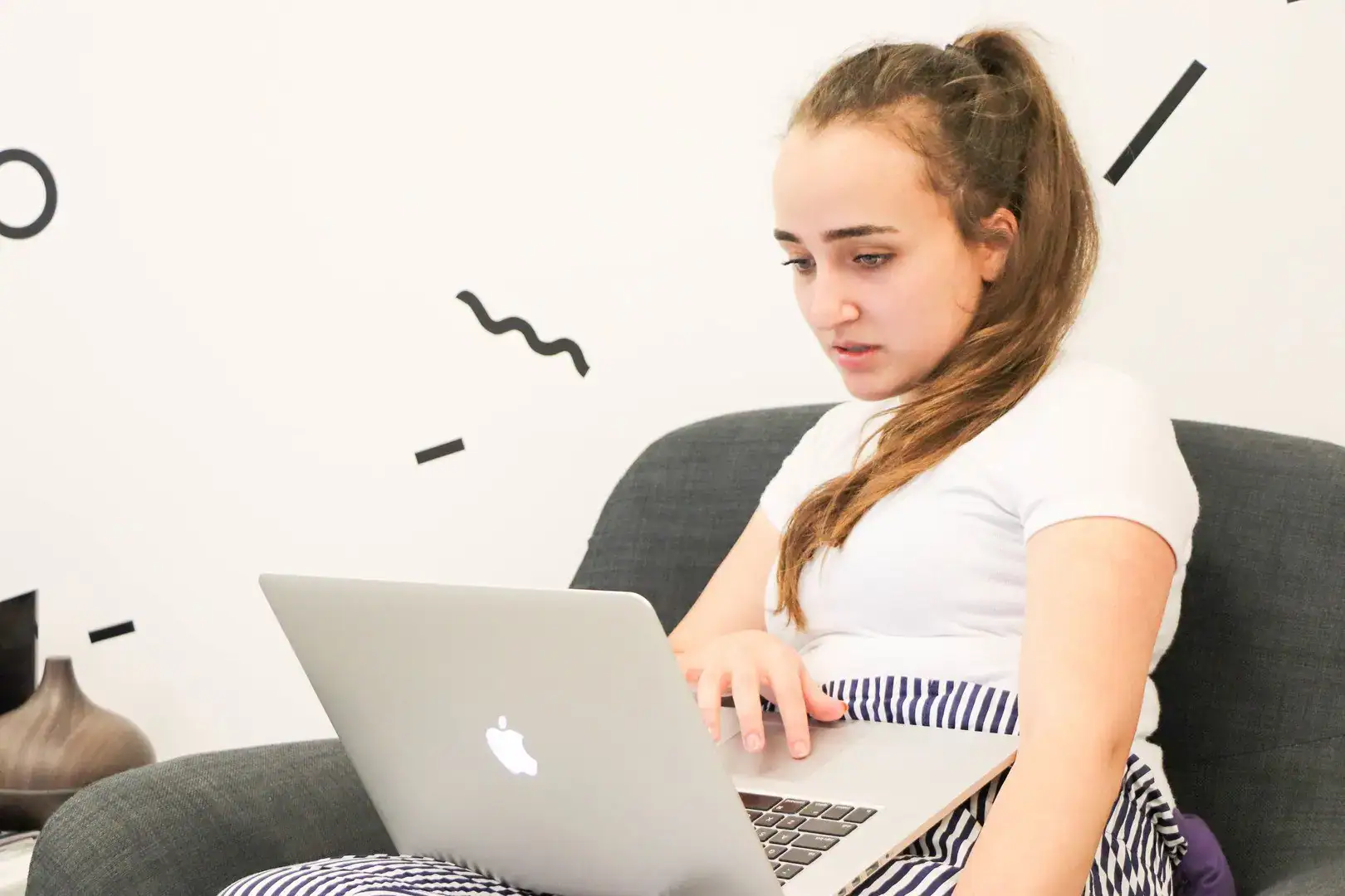 Young woman working on a laptop on a sofa.