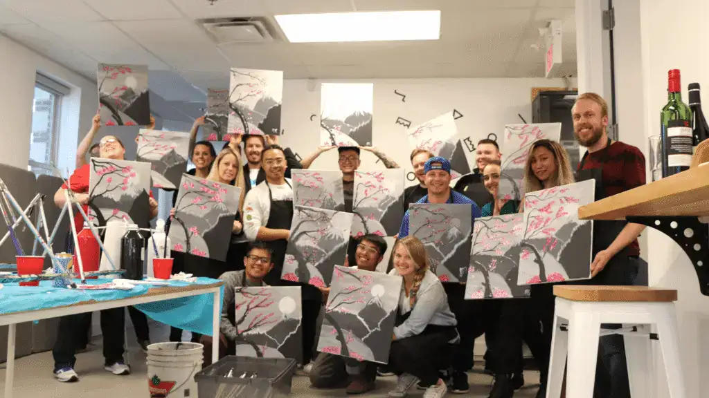 Group of people holding up their completed paintings at an art class.