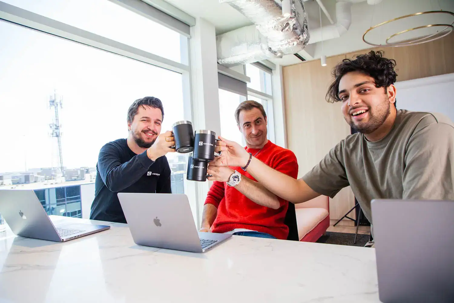 Team of young professionals clinking coffee cups during a meeting in a bright, modern office.