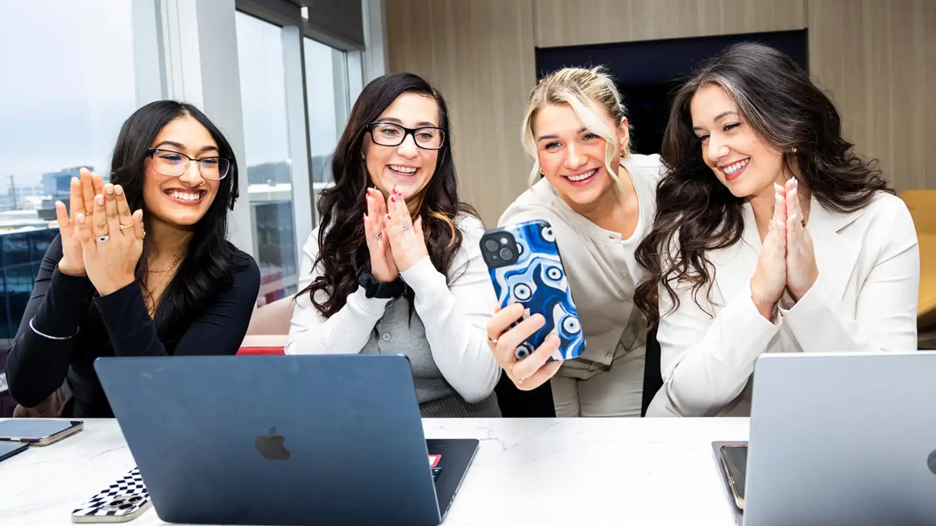 Women celebrating success during a virtual meeting in a modern office setting.