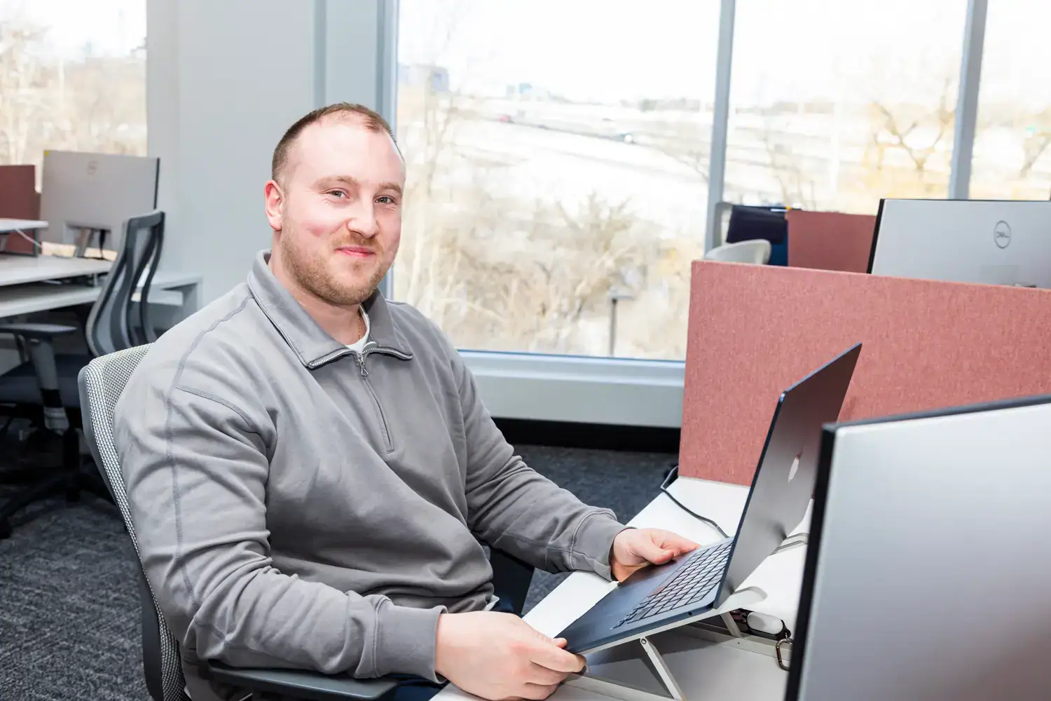 Man working on a laptop in an office setting with large windows.