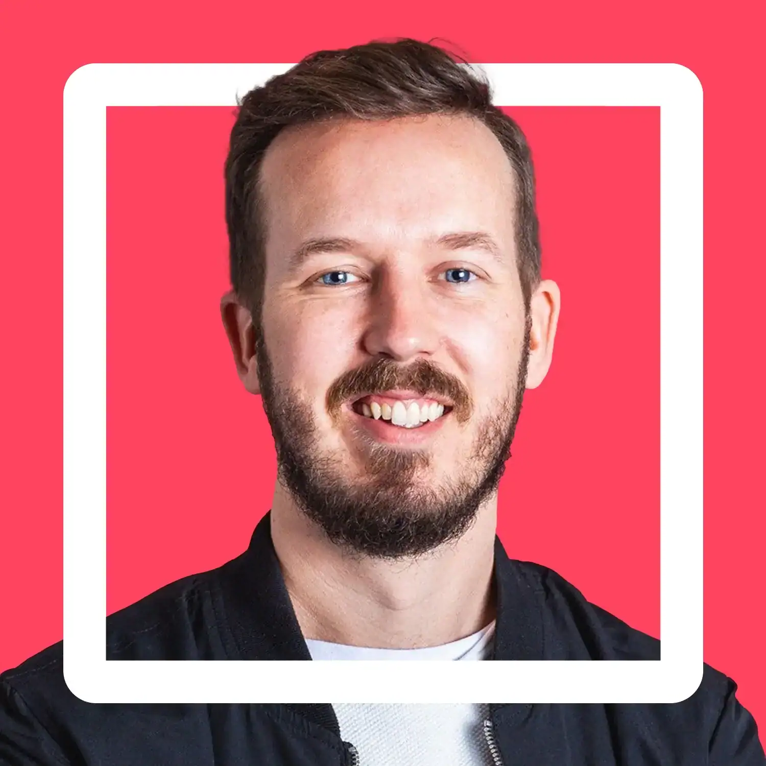 Young man smiling with beard and blue eyes on pink background.