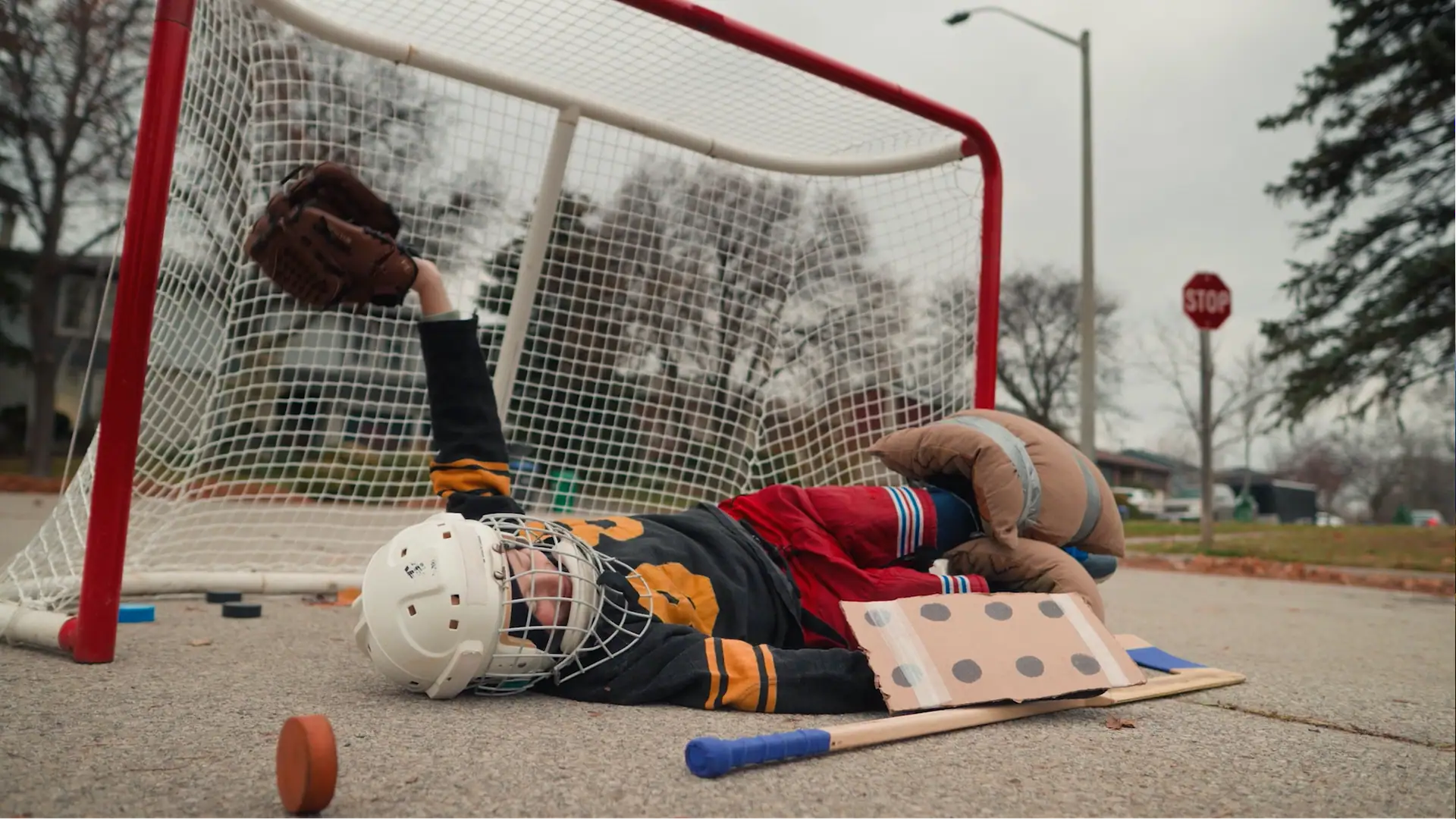 Child practicing hockey goalie save outside with hockey equipment.