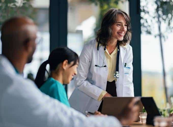 cription A cheerful doctor consults with a diverse medical team around a table, using tablets and charts