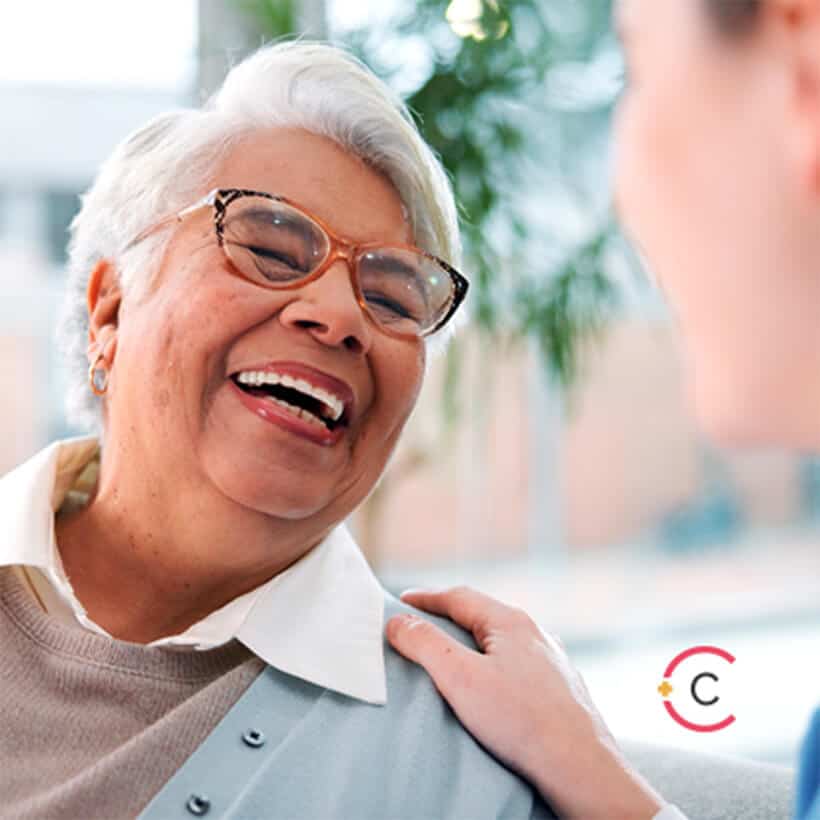 Elderly woman, nurse and laughing on sofa for funny conversation, medical support and bonding