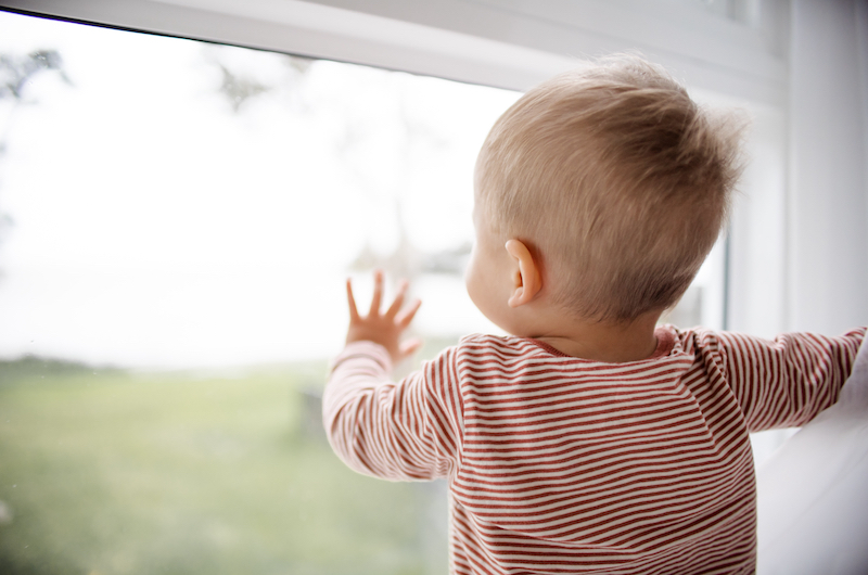 Kleinkind vor Fensterscheibe