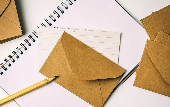 Briefumschläge aus Kraftpapier, Notizblock und Stift auf weißem Hintergrund.