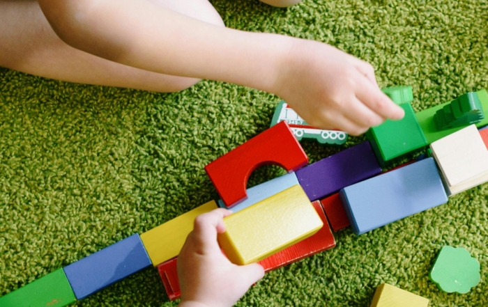 Kinder spielen mit bunten Bauklötzen auf grünem Teppichboden.