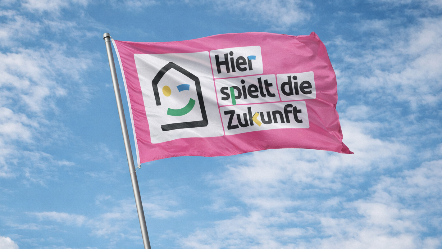 Ein farbenfrohes Banner mit dem Slogan "Hier spielt die Zukunft" weht im Wind vor einem blauen Himme.