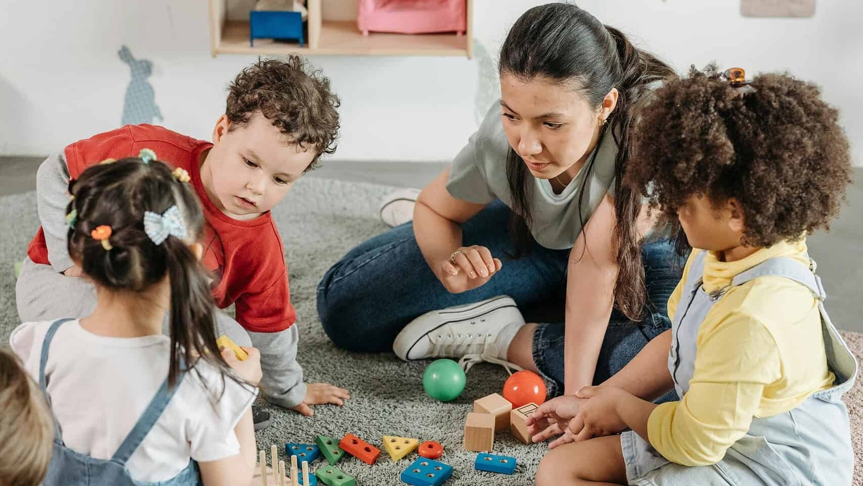 Kinder spielen mit bunten Bauklötzen und Bällen im Kindergarten, betreut von einer Erzieherin.