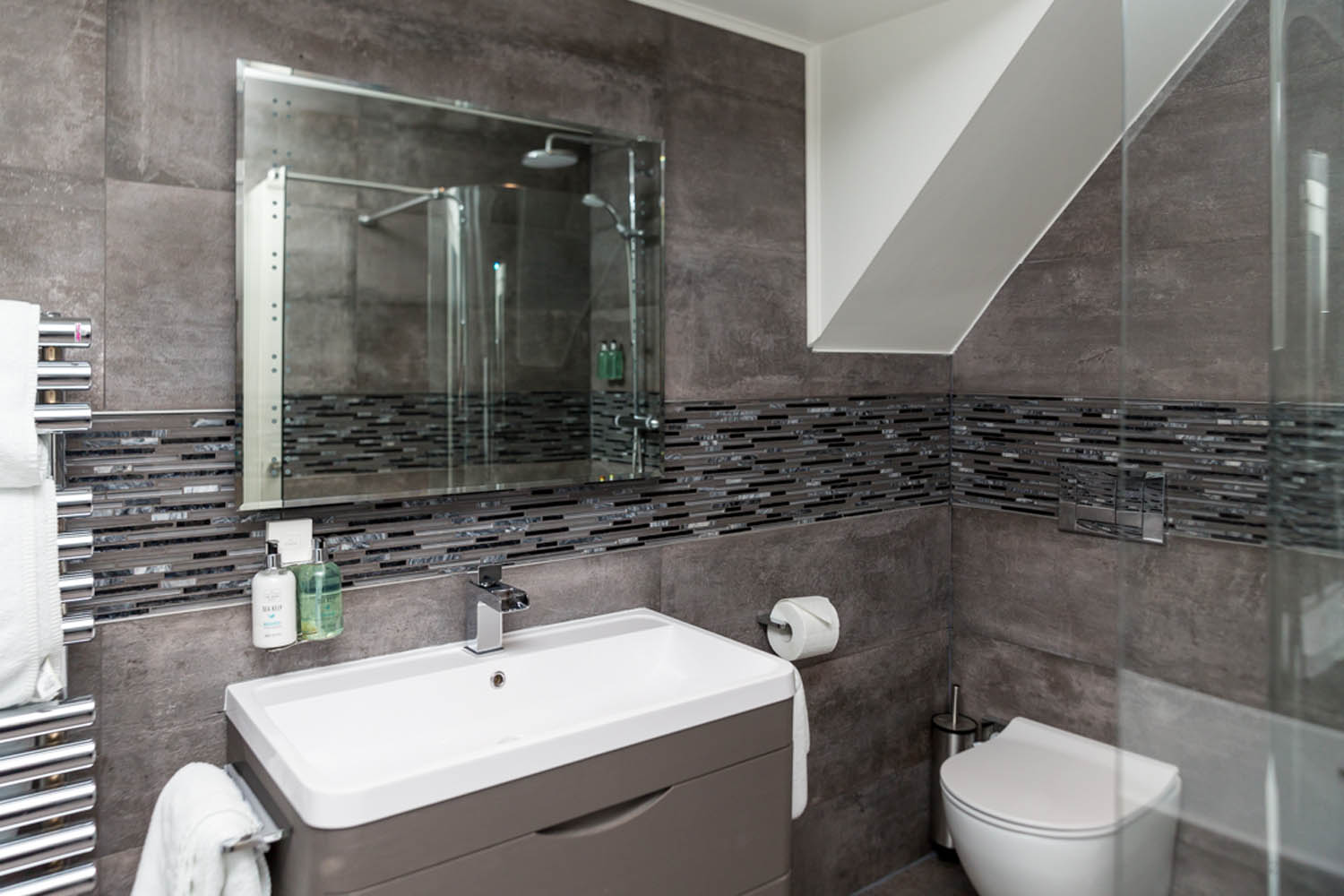 Modern bathroom with gray tiles, glass shower, and white fixtures at The Dowans Hotel.