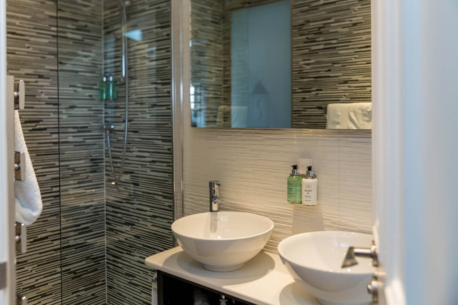 Modern bathroom with dual sinks and a glass-enclosed shower at The Dowans Hotel.