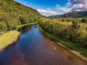 Serene river flowing through lush green woodland at Erchless Castle Estate Scotland.