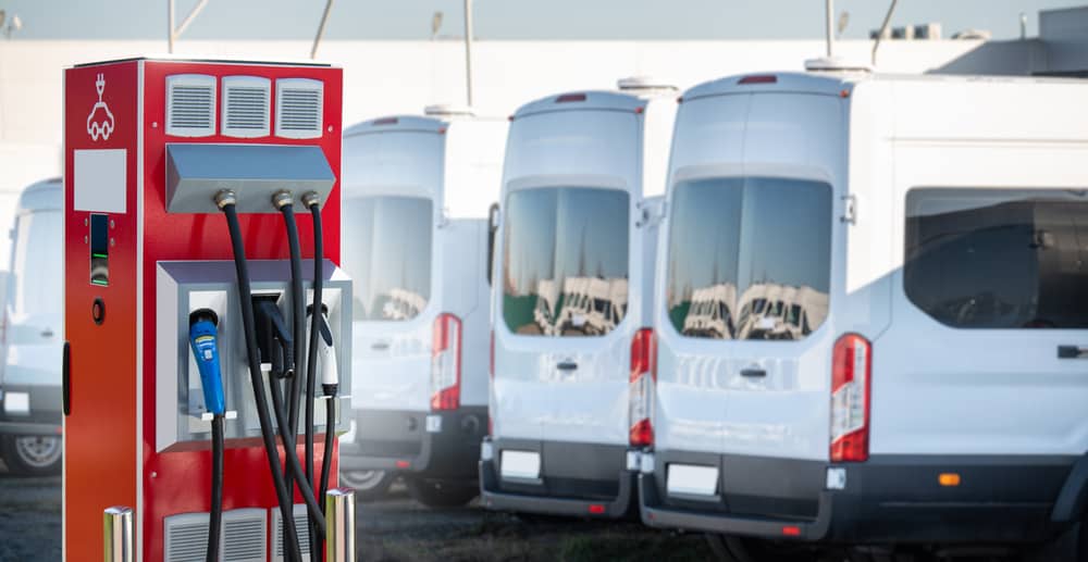Fleet of electric vans charging at EV station for sustainable transport.