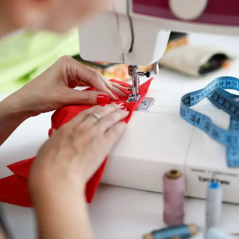 Stunning image of a person sewing vibrant red fabric with a sewing machine, surrounded by measuring tape and sewing tools, highlighting bespoke tailoring and fabric craftsmanship.