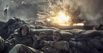 "Two soldiers in combat uniforms take cover behind sandbags as an explosion erupts nearby on a smoky, chaotic battlefield, with flames and debris filling the air."