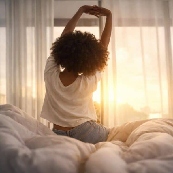 Woman stretching in morning sunlight with curtains behind her.