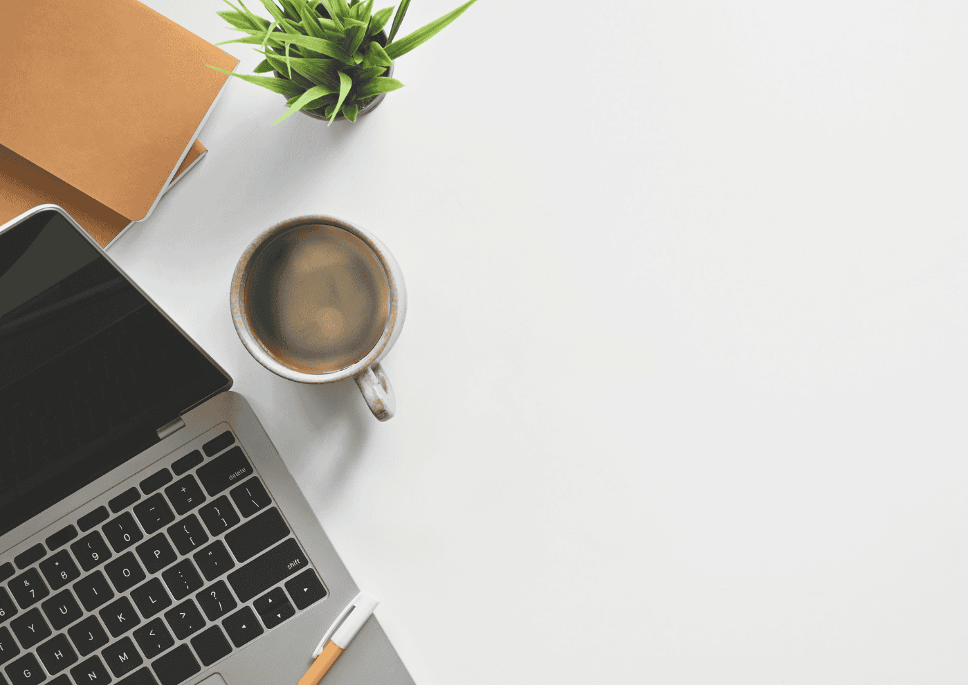 Work desk featuring a laptop, a cup of coffee, a small potted plant, and a notebook on a clean white surface.
