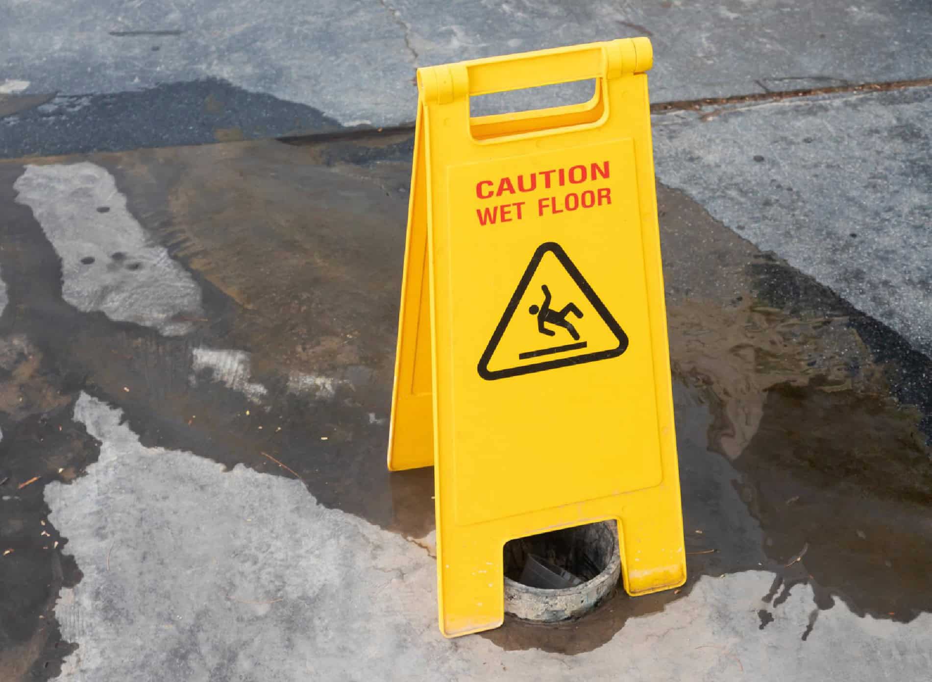 Caution wet floor sign on wet pavement highlighting a slippery surface hazard.