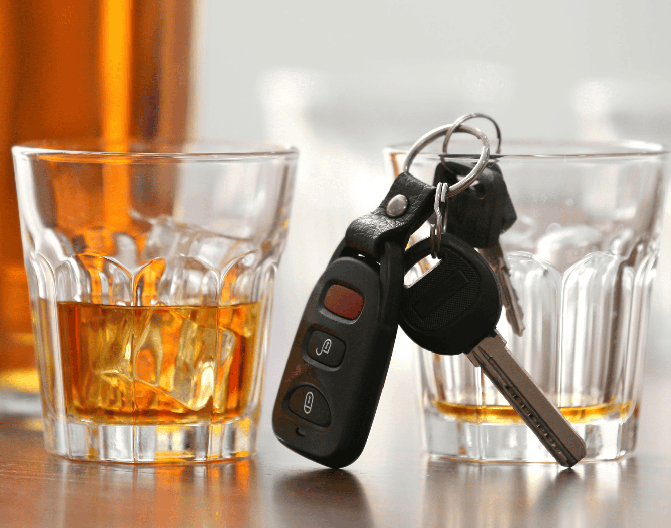 Close-up of whiskey glasses with ice and a set of car keys on a wooden table, highlighting a relaxed drinking scene.