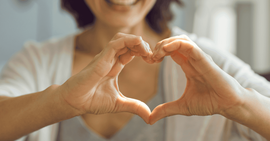 Person forming a heart shape with hands for community care.