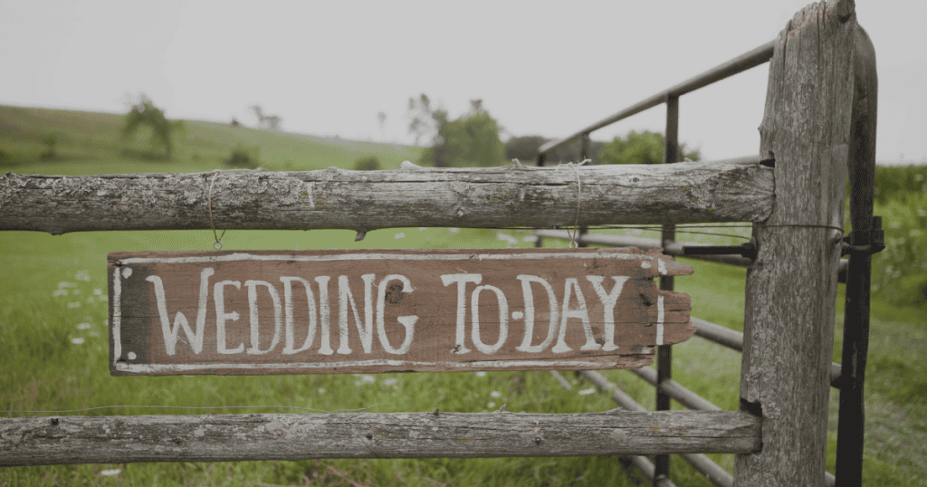 Rustic wooden fence with a wedding sign hanging, outdoor setting.