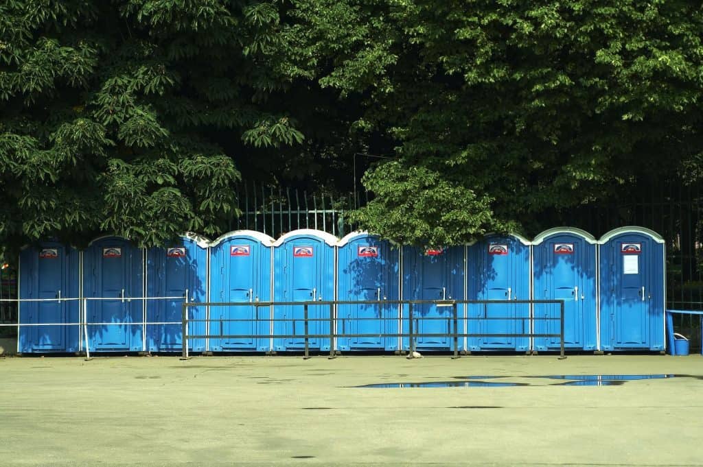 Row of blue portable restrooms on a sports field with trees in the background.