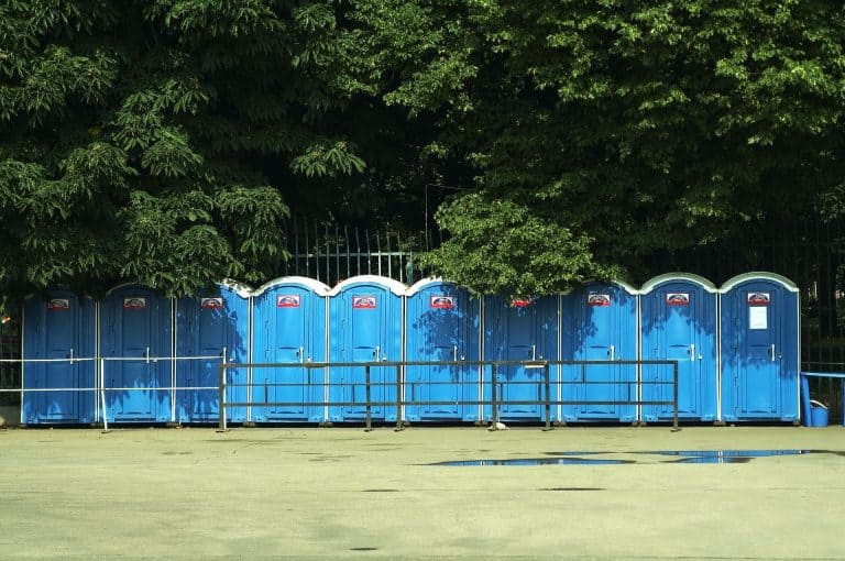 Row of blue portable restrooms on a sports field with trees in the background.