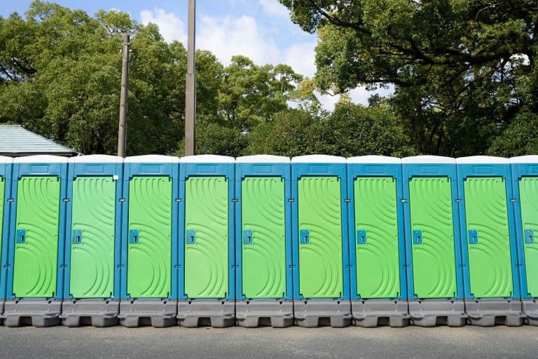 Line of portable restroom trailers with green doors and blue roofs.