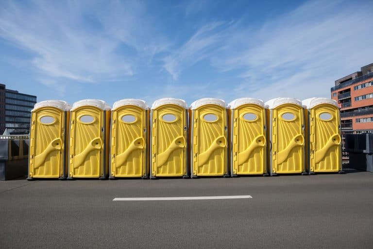 Row of yellow portable restroom trailers on city street under blue sky.