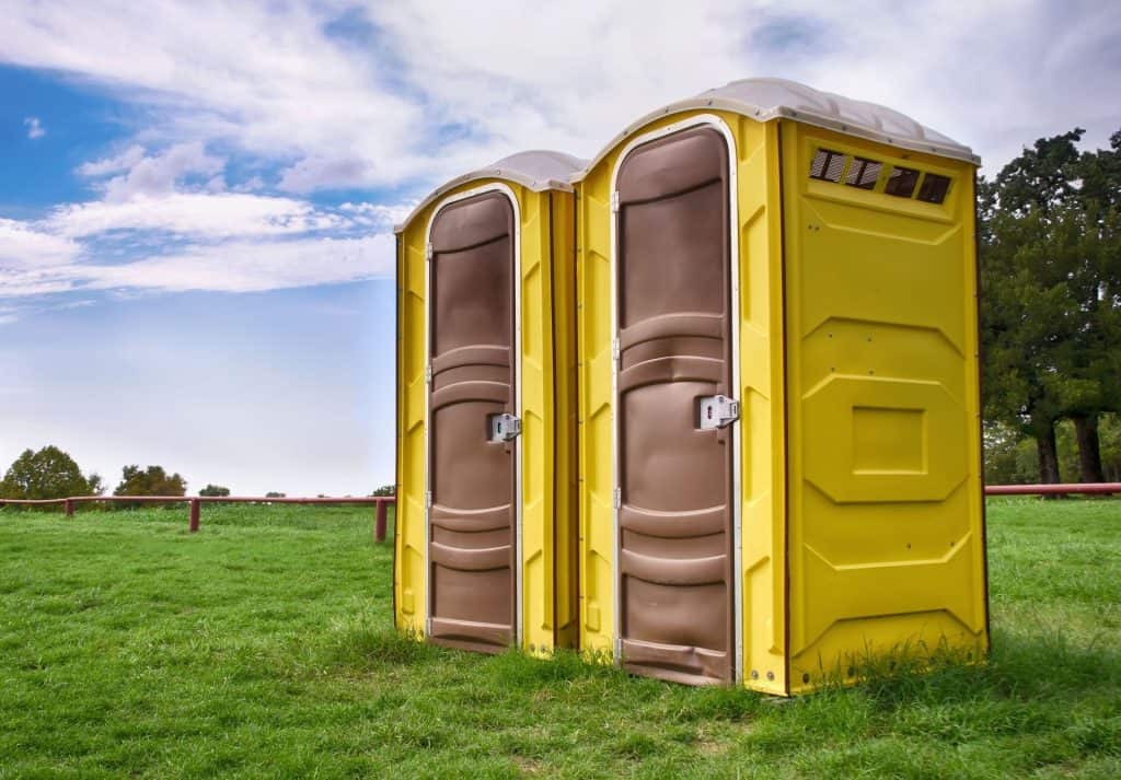 Two yellow portable restrooms on a grassy field with trees and sky in background.