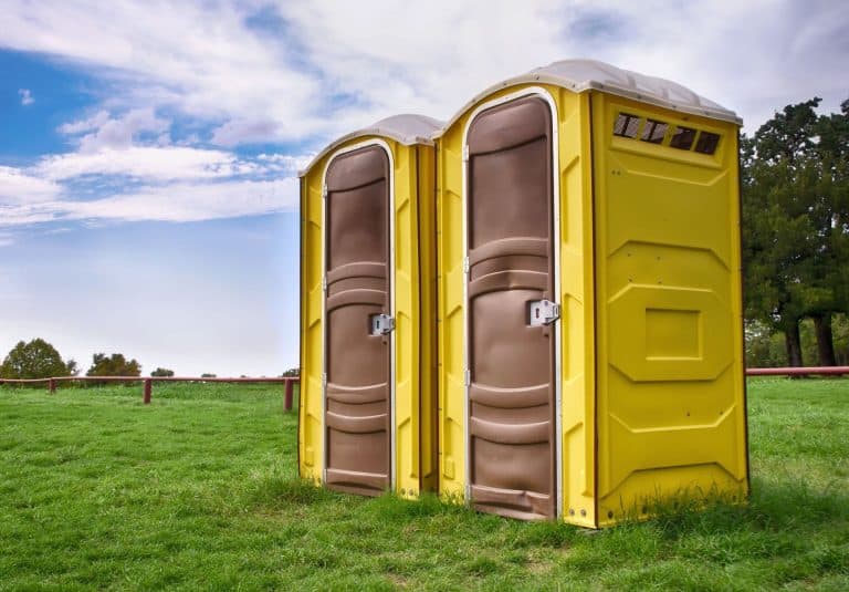 Two yellow portable restrooms on a grassy field with trees and sky in background.