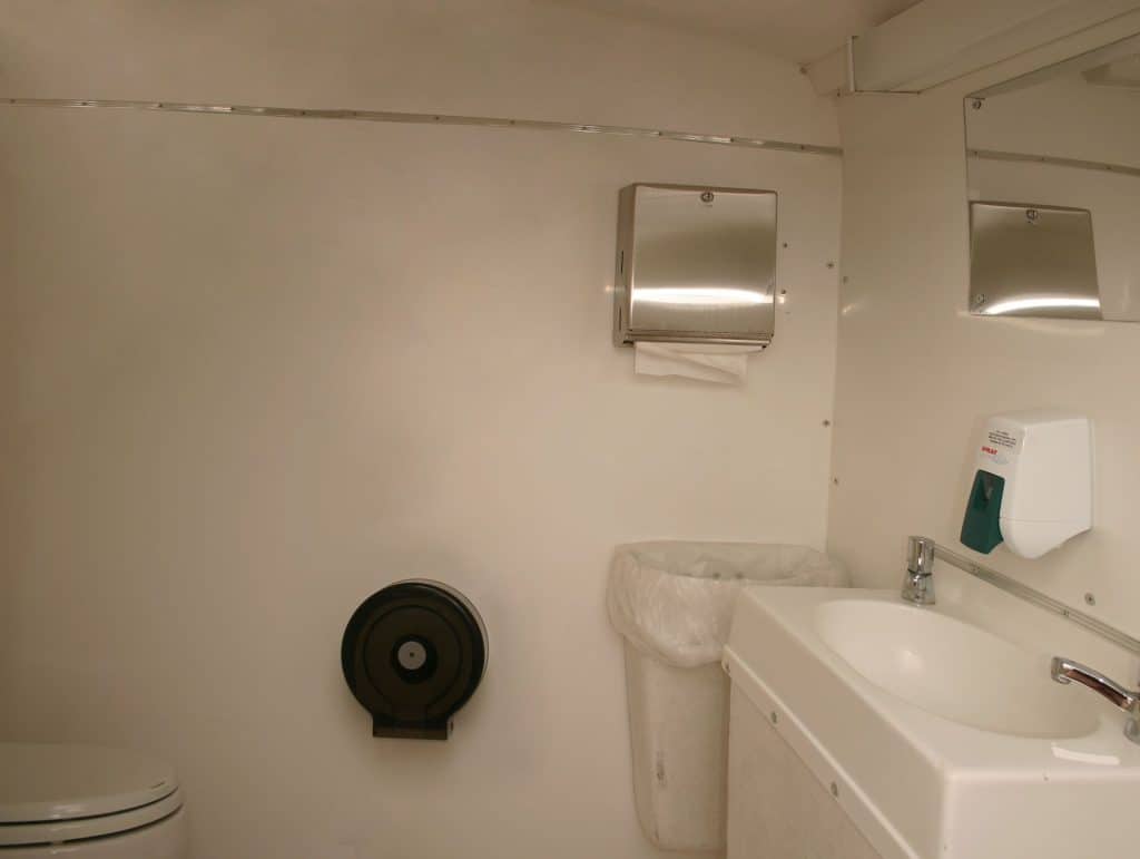 Modern portable restroom with sink, mirror, and hand dryer for events.