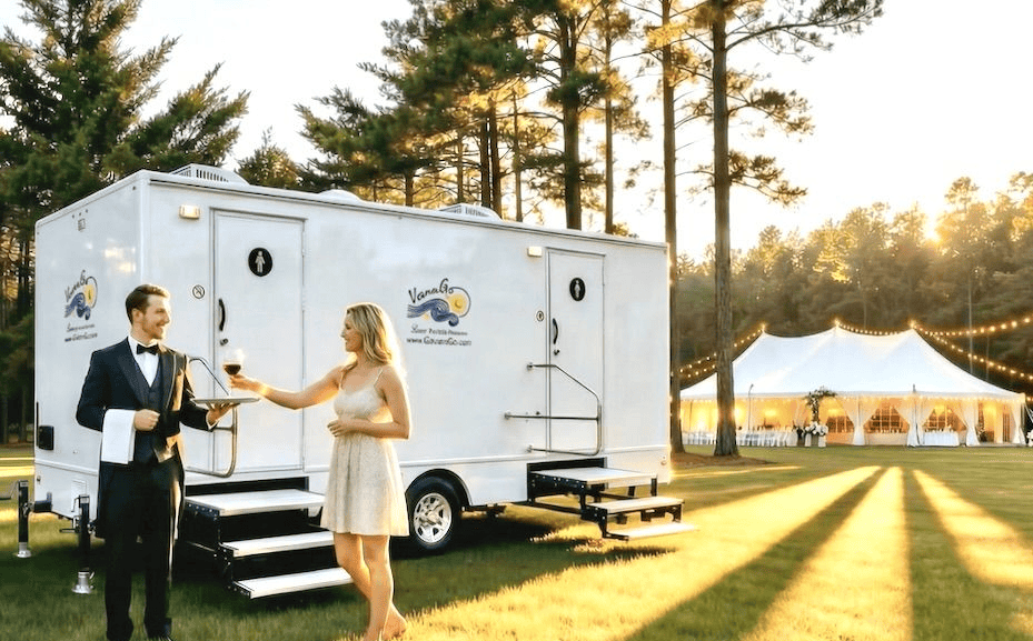 Luxury portable restroom trailer at outdoor event with sunset and tent in background.