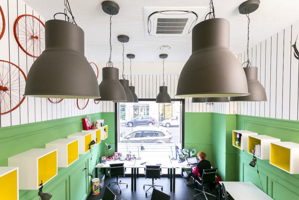 Modern coworking space with green walls and large pendant lights.