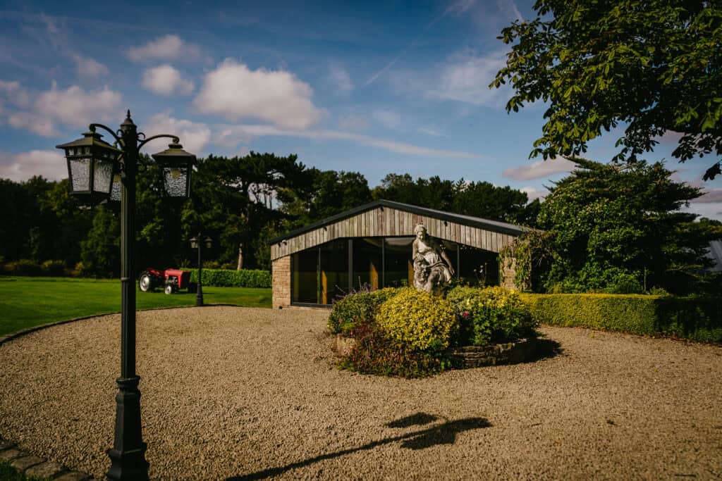 Hyde Bank Farm barn entrance with a modern building and a stone sculpture, surrounded by greenery.