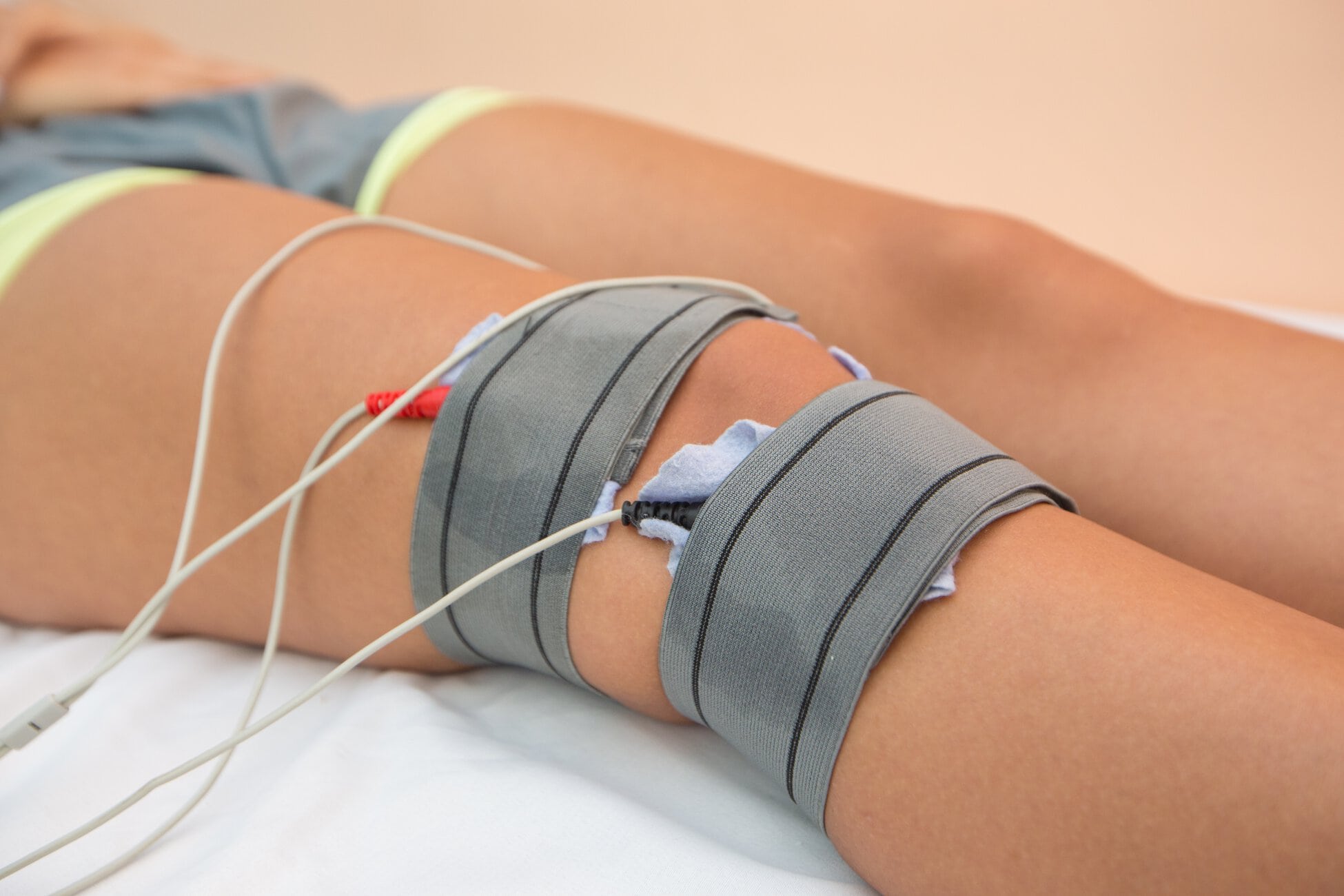 Close-up of a leg with medical straps and electrode wires attached for monitoring while lying on a bed.