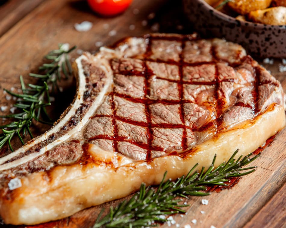 Grilled T-bone steak with grill marks on a wooden board, garnished with rosemary sprigs.