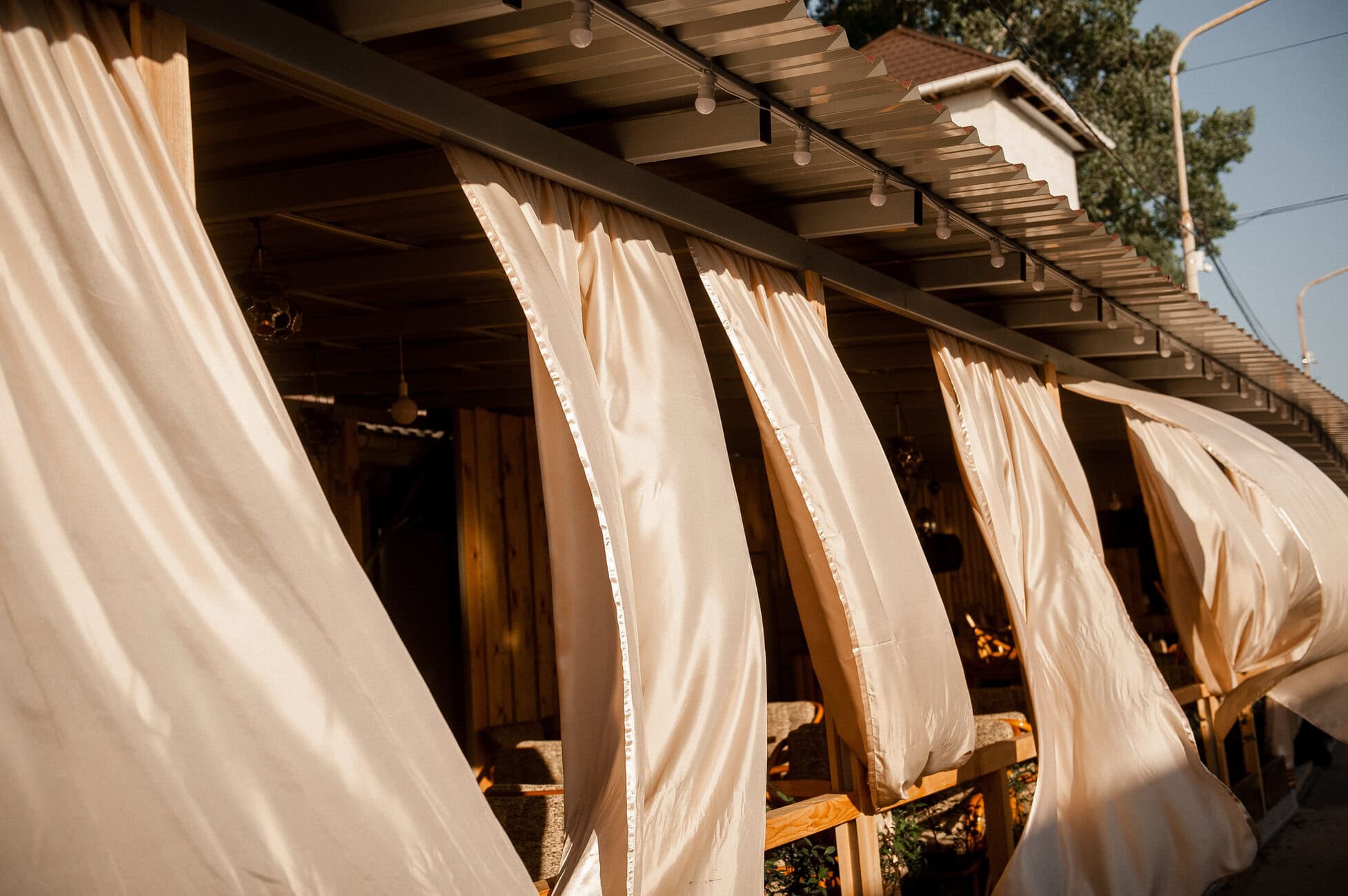 Beige curtains billowing along an outdoor dining area under a covered patio.