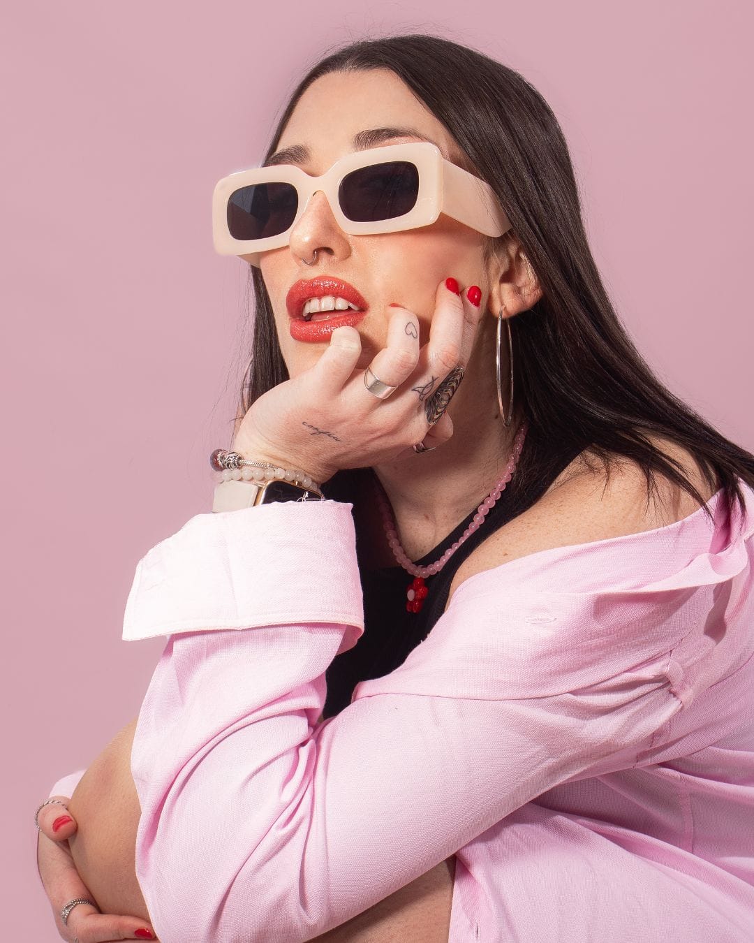 Portrait of a stylish person wearing oversized pink sunglasses, pink shirt, and red lipstick against a pink backdrop