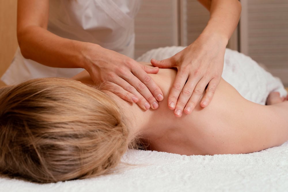 Therapist kneading a client’s upper back while they lie face down on a massage table in a spa setting