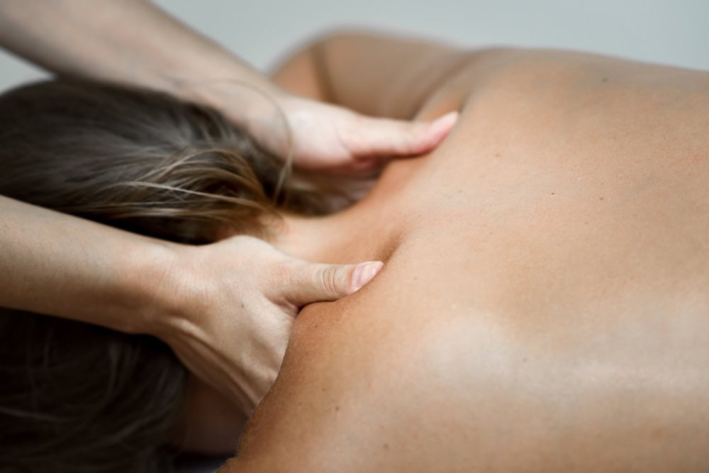 Close-up of a massage therapist's hands kneading a client's upper back and neck during a massage.