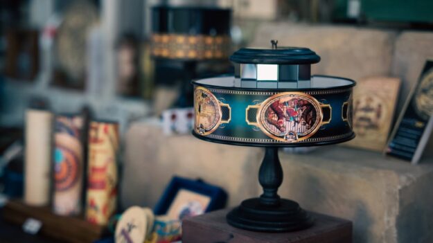 Decorative vintage lamp on a dark pedestal in a shop, featuring a teal band with gold medallions.
