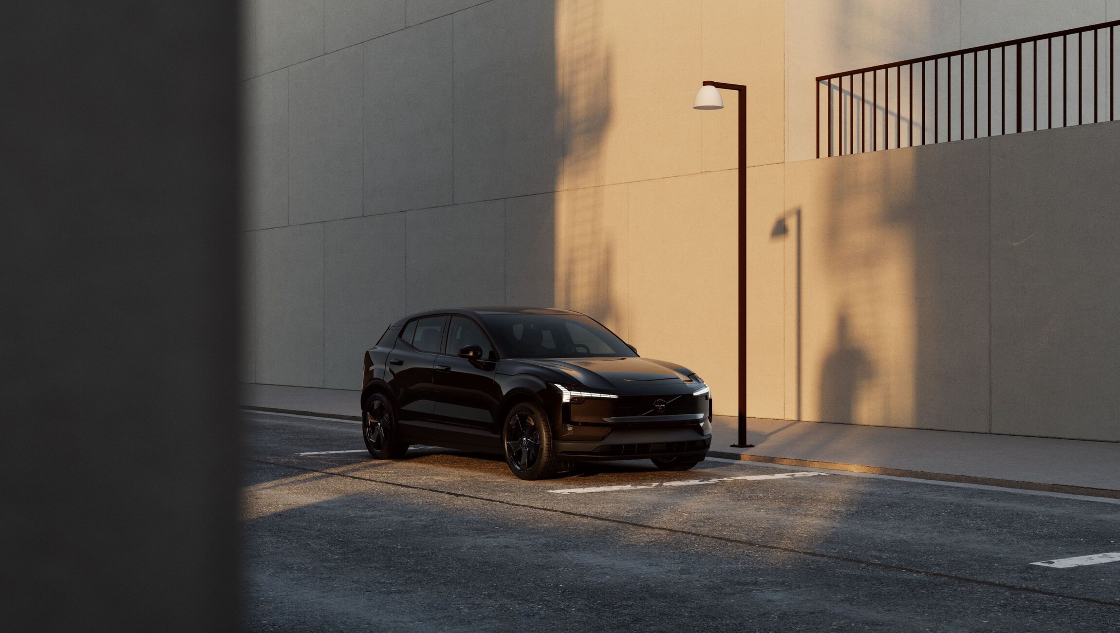 Black SUV parked along a sunlit concrete wall at dusk beside a streetlamp casting long shadows