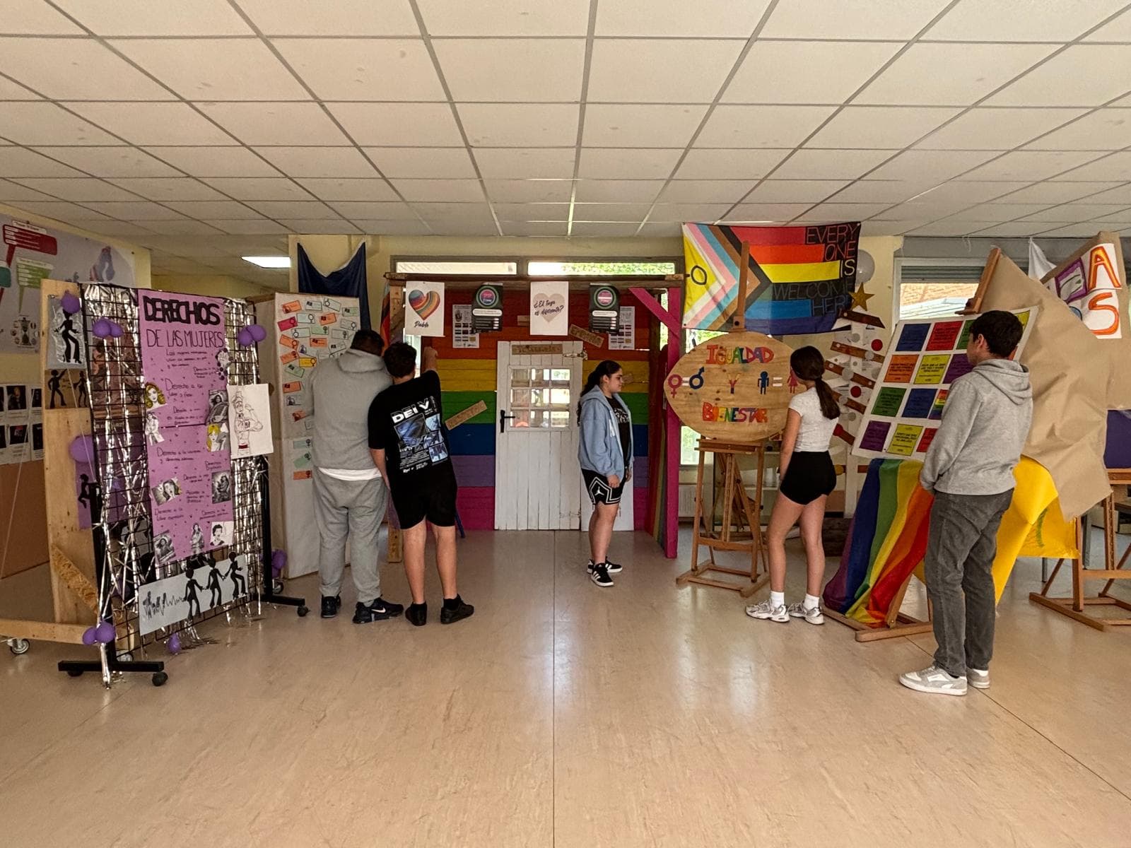 Students explore a hallway exhibit with colorful posters and rainbow decorations about diversity and inclusion.